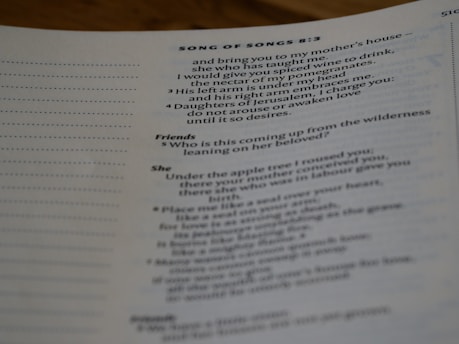 A close-up view of a page from a book, featuring text from the Bible, specifically Song of Songs 8:3. The text is presented in a structured format, with section headings such as 'Friends' and 'She'. The focus is mainly on the center and right side of the page.
