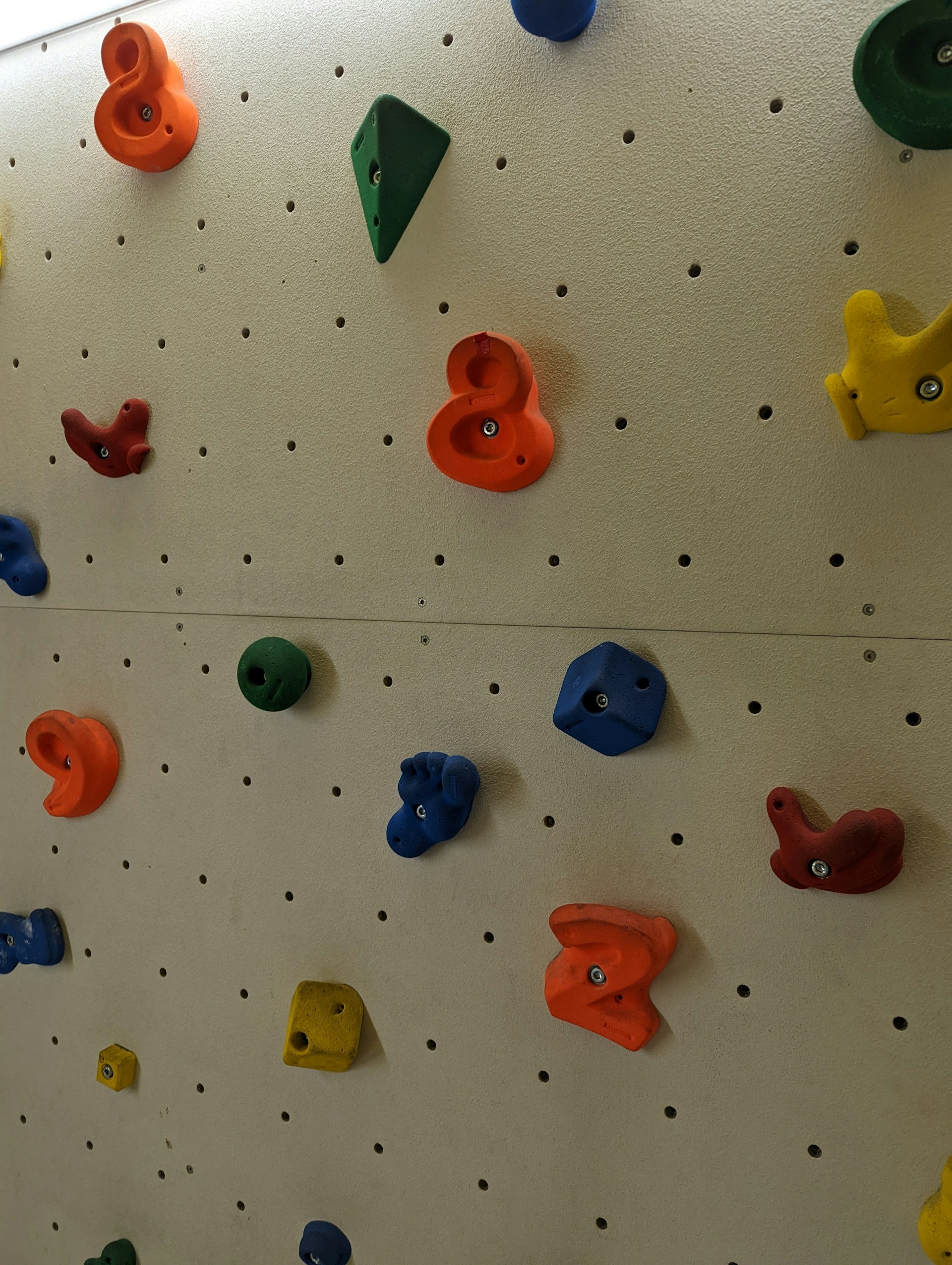 A close-up of hands gripping colorful climbing holds on a gym wall, showcasing various textures.
