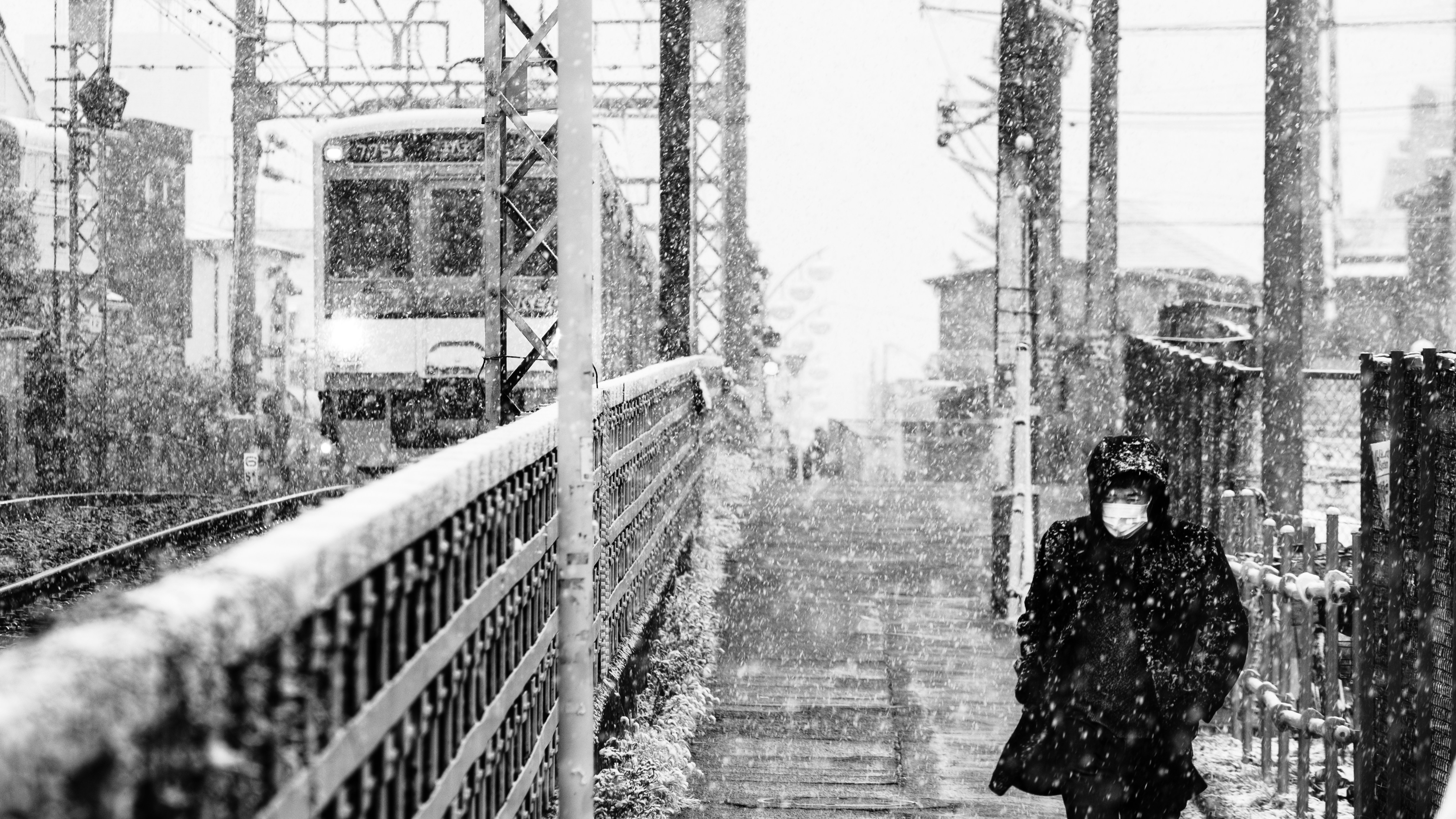 a person walking on a sidewalk, Man walking at the beginning of snow storm next to train