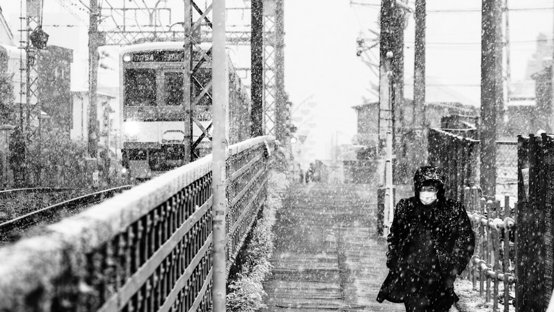 a person walking on a sidewalk, Man walking at the beginning of snow storm next to train