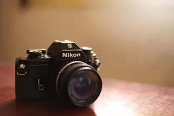 A vintage Nikon camera resting on a wooden surface, capturing the essence of classic photography. The lens is prominently featured, with a focus on the brand logo. Soft lighting creates a warm and nostalgic atmosphere, highlighting the textured details of the camera body.
