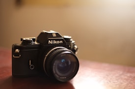 A vintage Nikon camera resting on a wooden surface, capturing the essence of classic photography. The lens is prominently featured, with a focus on the brand logo. Soft lighting creates a warm and nostalgic atmosphere, highlighting the textured details of the camera body.
