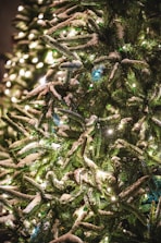 Snow gently falling over a brightly lit Christmas tree outdoors.