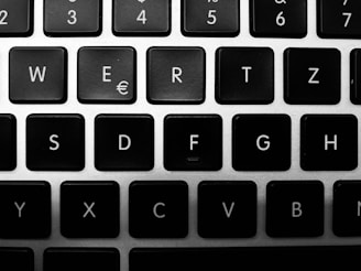 A close-up view of a black and white keyboard, featuring keys with white letters, symbols, and numbers on top of dark keys on a silver frame.