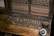 A vintage telephone switchboard featuring numerous metal jacks and plugs, with a rotary dial on the side. The equipment has a worn, wooden surface and metallic components that appear aged and tarnished.