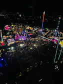 Nighttime amusement park scene illuminated by glowing rides and festive colorful lights.