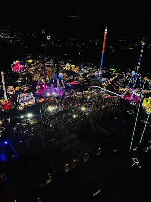 Nighttime amusement park scene illuminated by glowing rides and festive colorful lights.