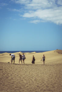 A group trekking across golden sand dunes under a clear blue sky.