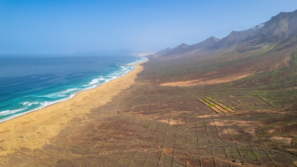 a sandy beach with a body of water and hills in the background