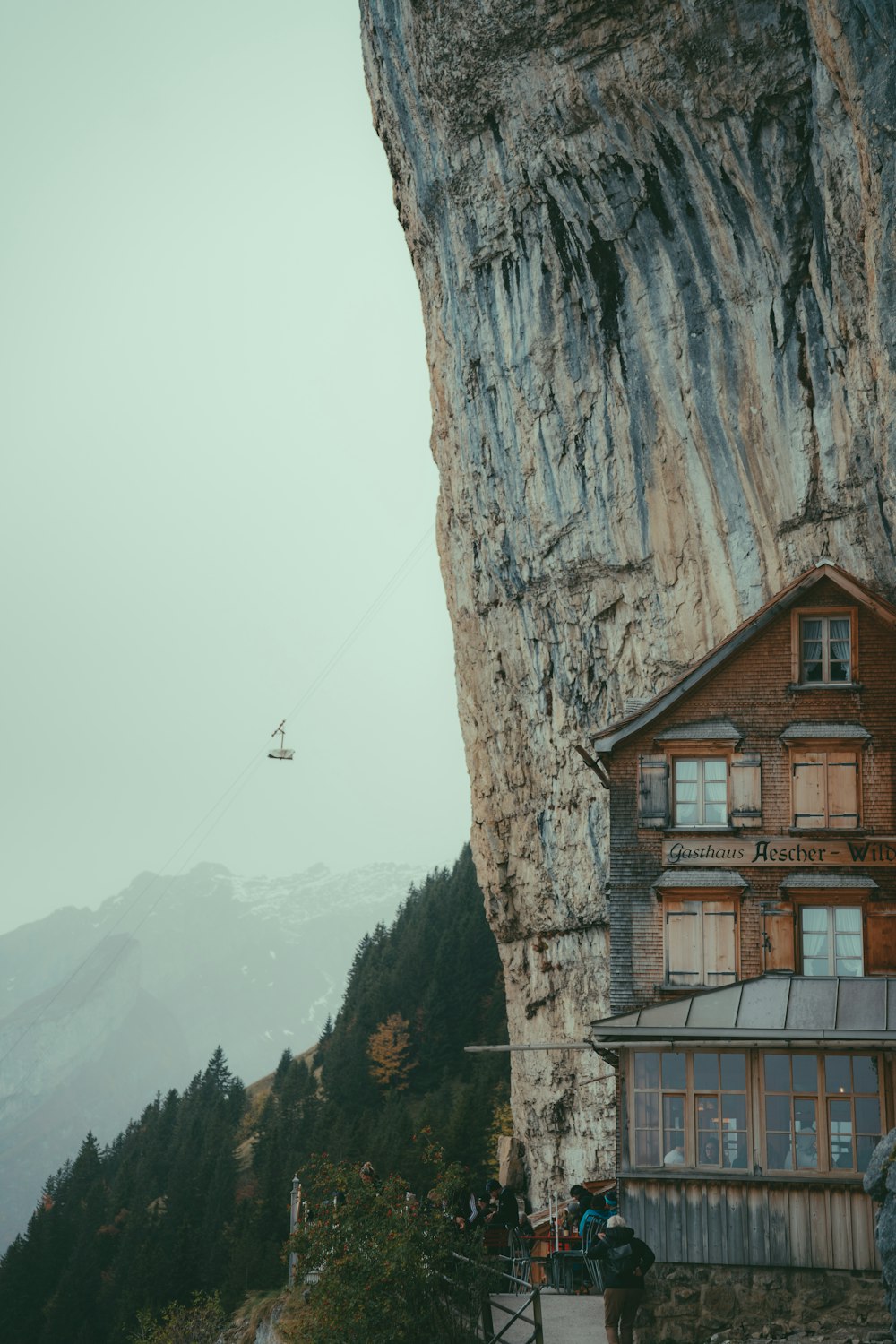 a cliff side with a building and a helicopter flying in the sky