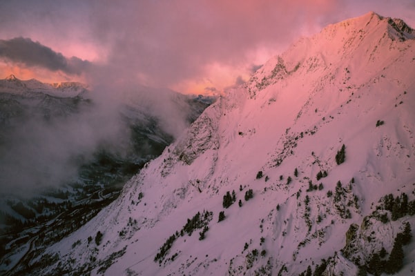 Pink alpenglow lighting a rugged snow-plastered Wasatch ridgeline above drifting cloud