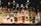 A collection of assorted liquor bottles is arranged on a backlit shelf. The bottles vary in shape, size, and color, featuring well-known brands like Absolut, Bacardi, Martini, and Jägermeister. The background is dimly lit, creating a reflective and ambient setting.