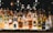 A collection of assorted liquor bottles is arranged on a backlit shelf. The bottles vary in shape, size, and color, featuring well-known brands like Absolut, Bacardi, Martini, and Jägermeister. The background is dimly lit, creating a reflective and ambient setting.