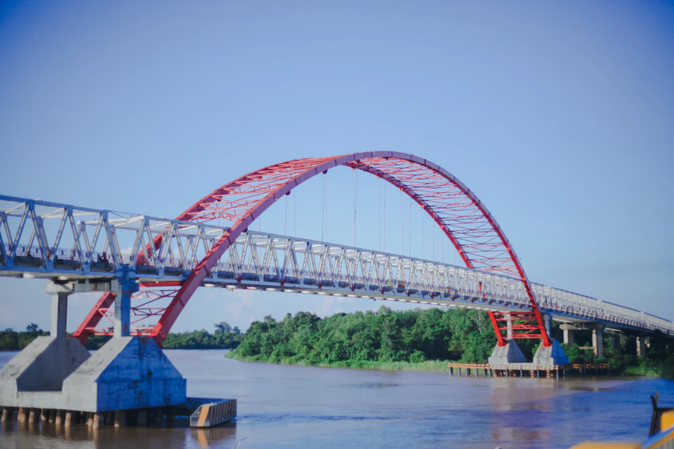Striking red and white arch bridge spans across a river with two concrete pillars
