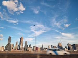 Photo of a modern city skyline with construction cranes and a sleek car showroom in the foreground.