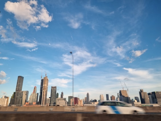 Photo of a modern city skyline with construction cranes and a sleek car showroom in the foreground.