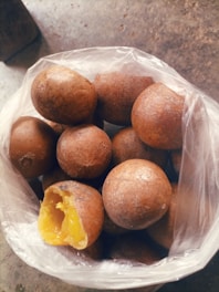 A collection of brown, round fruits with a rough exterior is placed inside a translucent plastic bag. One of the fruits has been partially eaten, revealing a bright yellow interior.