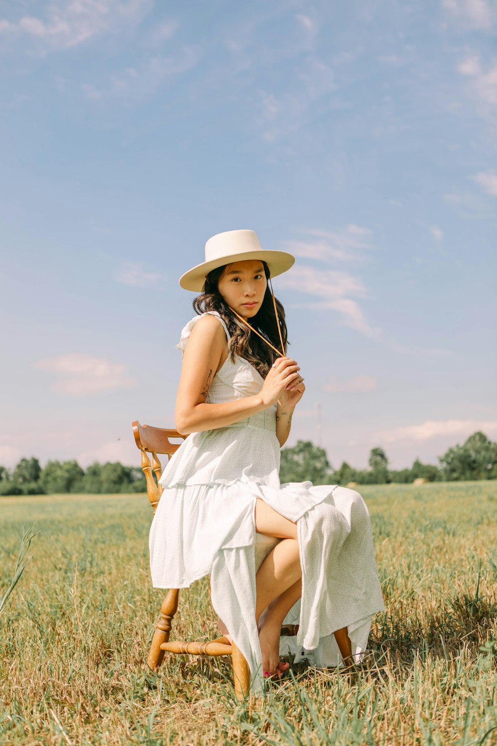 Eine Person in weißem Kleid und Hut sitzt auf einem Feld