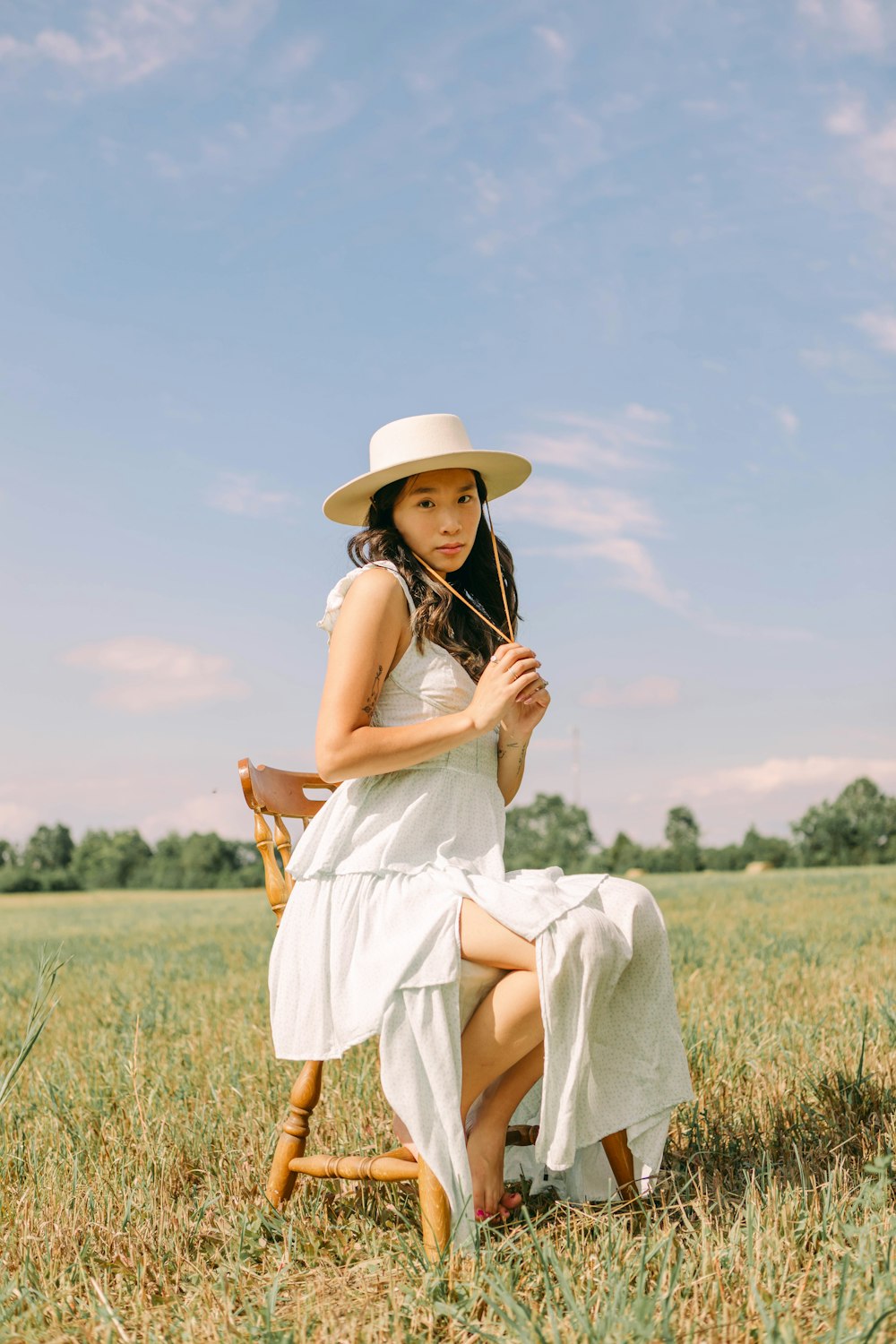 a person in a white dress and hat sitting in a field