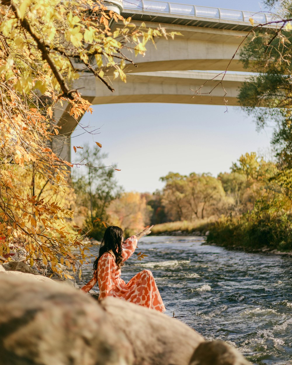 a person sitting on a rock by a river with a bridge in the background