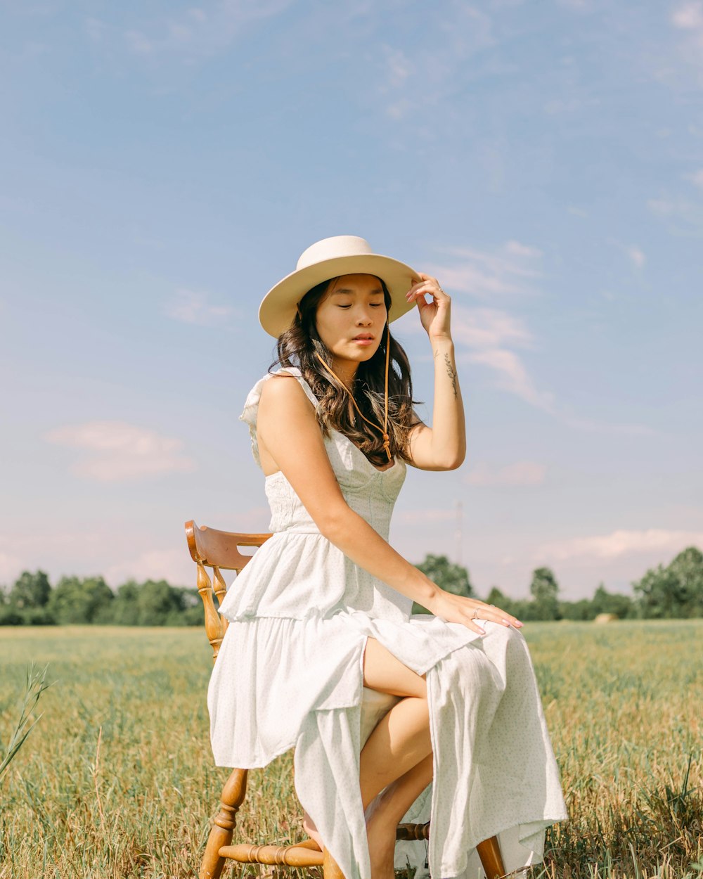 a person in a white dress and hat sitting in a field