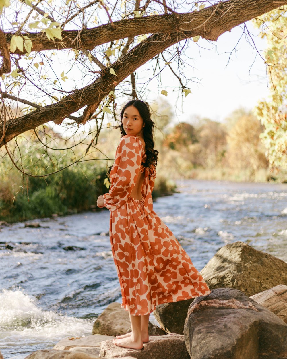 a person in a dress standing on rocks by a river