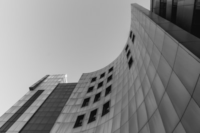 A modern building with a curved, sleek architectural design, featuring a series of rectangular windows. The facade is composed of panels, reflecting a minimalist and contemporary style.