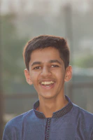 A cheerful young person wearing Modaviva apparel, smiling outdoors with city buildings blurred behind.