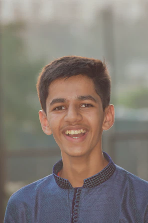 A cheerful young person wearing Modaviva apparel, smiling outdoors with city buildings blurred behind.