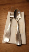 Close-up of a napkin embroidered with a family crest, resting on a polished dining table with silver cutlery.