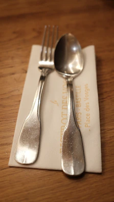 Close-up of a napkin embroidered with a family crest, resting on a polished dining table with silver cutlery.