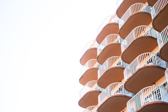 A series of balconies with curved railings extend from a building, creating a repetitive geometric pattern. The balconies are shaded in warm tones and contrast against a bright, clear sky.