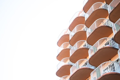 A series of balconies with curved railings extend from a building, creating a repetitive geometric pattern. The balconies are shaded in warm tones and contrast against a bright, clear sky.