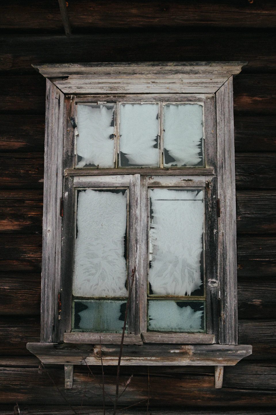 Close-up view of a weathered wooden window with six panes and white frame