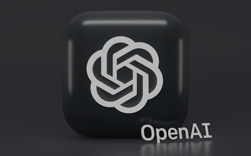 A 3D-style logo with a geometric design is prominently displayed on a dark, rounded square background. Below the logo, the word 'OpenAI' is written in a sleek, modern font.