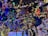 A festive ceiling adorned with colorful Christmas lights, whimsical elf decorations, and vibrant wreaths. Striped ornaments and plush elf legs hang playfully, with a prominent gift box featuring a hashtag on the right.