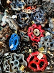 A collection of colorful, metal valve handles in various shapes and sizes piled together. Each handle is labeled with a price tag, indicating they might be for sale or display. The vibrant colors include blues, reds, and blacks, creating a visually striking composition.