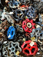 A collection of colorful, metal valve handles in various shapes and sizes piled together. Each handle is labeled with a price tag, indicating they might be for sale or display. The vibrant colors include blues, reds, and blacks, creating a visually striking composition.