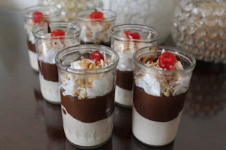 An elegant display of dessert shots in glass cups with creamy layers and delicate toppings, styled with soft pink and cream tones.