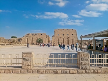 A group of diverse people gathered around ancient artifacts under a bright sky.