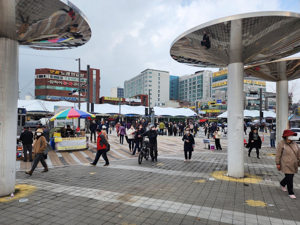 Un grupo de personas caminando alrededor de una gran plaza con tiendas de campaña y sombrillas