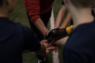 Team huddle with hands stacked, illuminated by sharp white and deep red lighting.