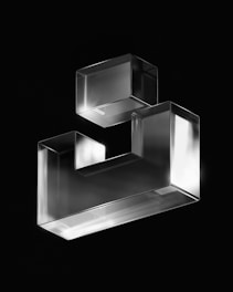 A sleek metal geometric sculpture with clean lines displayed on a minimalist shelf.