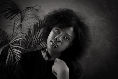 A warm editorial portrait of an African woman smiling confidently against a deep wine red backdrop.