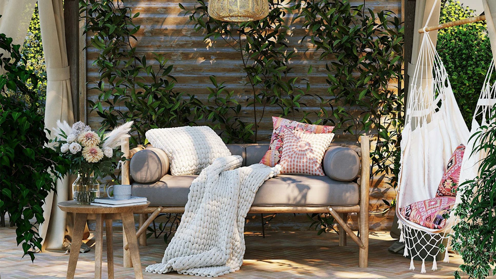 A cozy outdoor loveseat nestled in a sunlit garden corner with soft cushions and a woven throw.