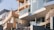 Modern residential buildings with large glass windows and brick facades are positioned on a rocky hill. The structures feature contemporary architectural elements such as balconies with glass railings. The use of natural rock and wood adds to the aesthetic.