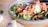 A close-up of the oil dispenser being used with a drizzle of oil on a salad.