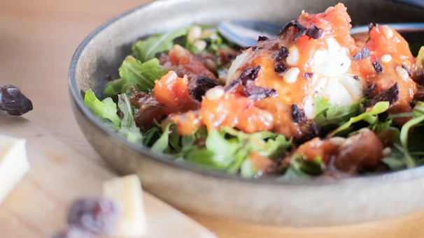 Close-up of a rich, dark balsamic dressing drizzling over fresh greens in a clear glass bottle.