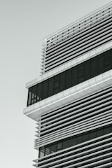 A modern architectural structure featuring a grid of horizontal and vertical lines. The building design incorporates glass and metal elements, with large windows and shading panels.