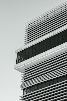 A modern architectural structure featuring a grid of horizontal and vertical lines. The building design incorporates glass and metal elements, with large windows and shading panels.
